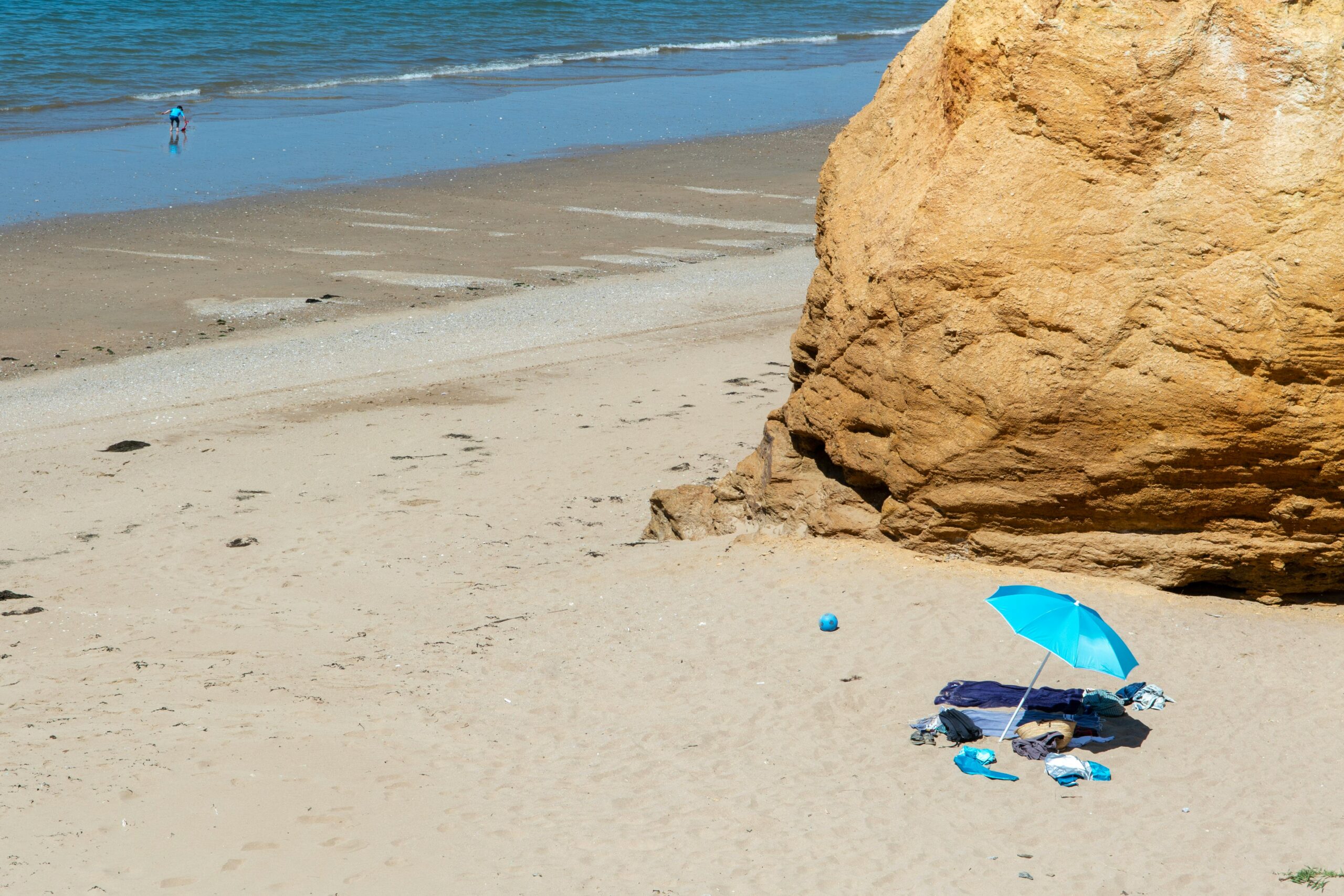 A serene beach scene with a vibrant blue umbrella and sandstone formation on a sunny day.