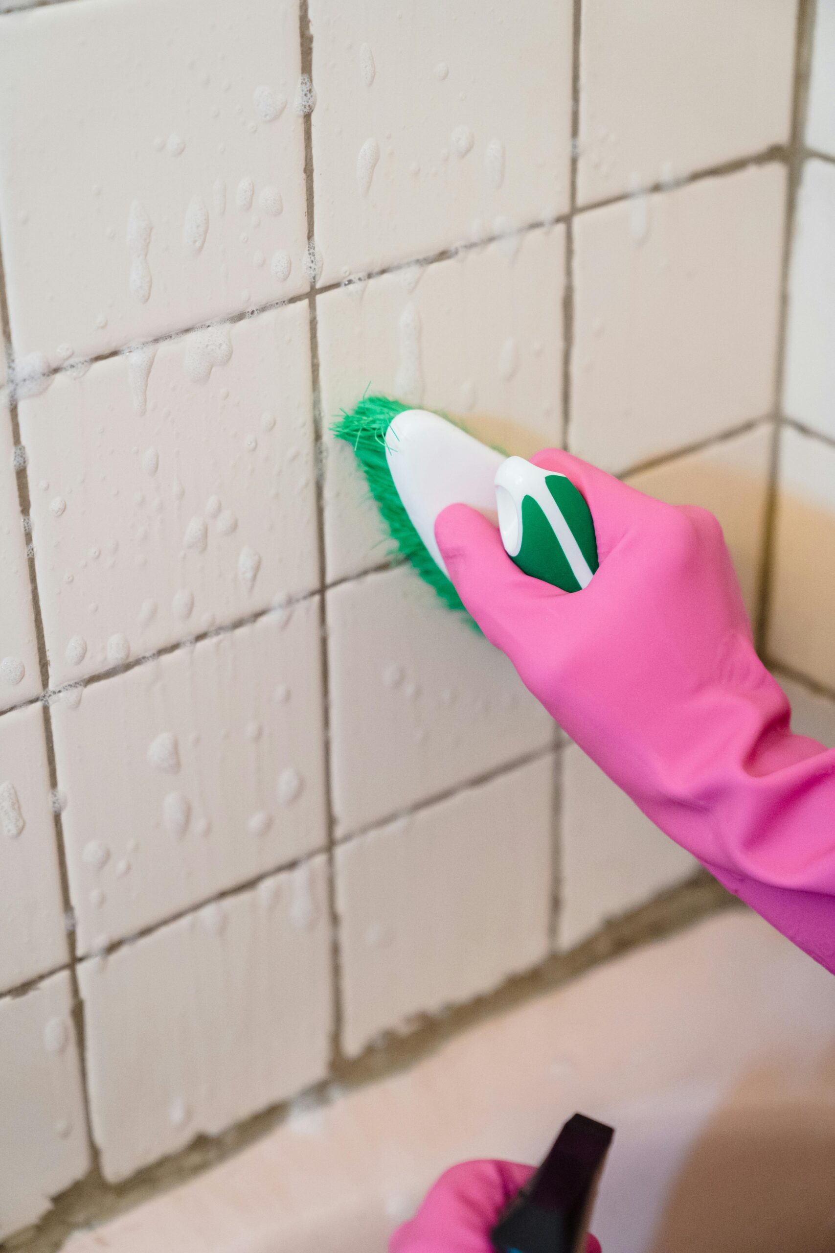 Preventing Household Accidents A hand in pink gloves scrubs bathroom tiles with a green brush to remove grime.